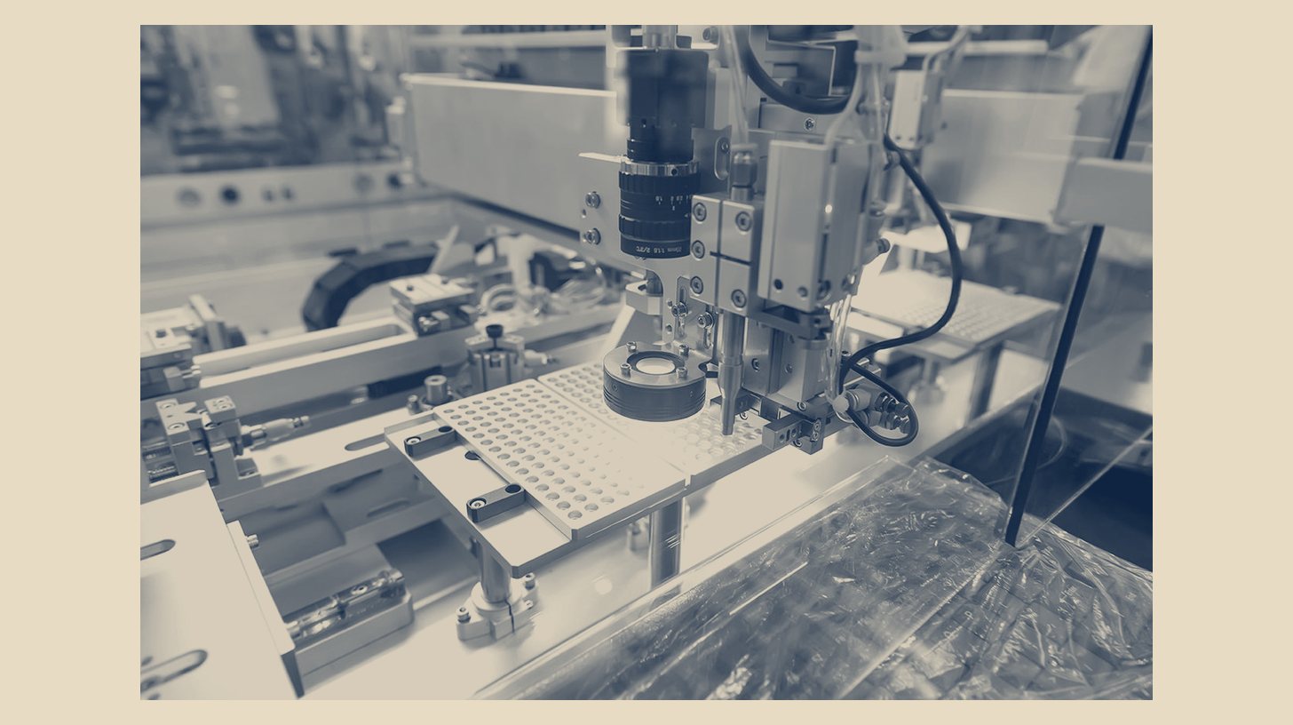 Two-tone Gooch & Housego company photo of an automated optics assembly cell on a production line, shown as a panel on a plain sand background.