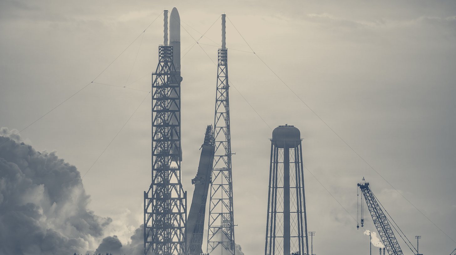Two-tone U.S. Space Force photo of a Blue Origin New Glenn rocket lifting off between its launch towers at Cape Canaveral on its third flight, April 19, 2026.