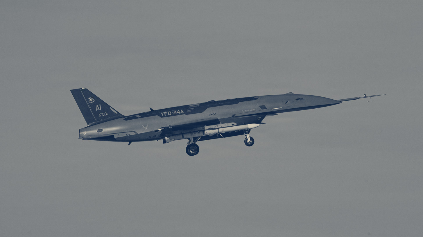 Two-tone photo of a YFQ-44A Collaborative Combat Aircraft in flight carrying inert stores during a captive-carry test over California.