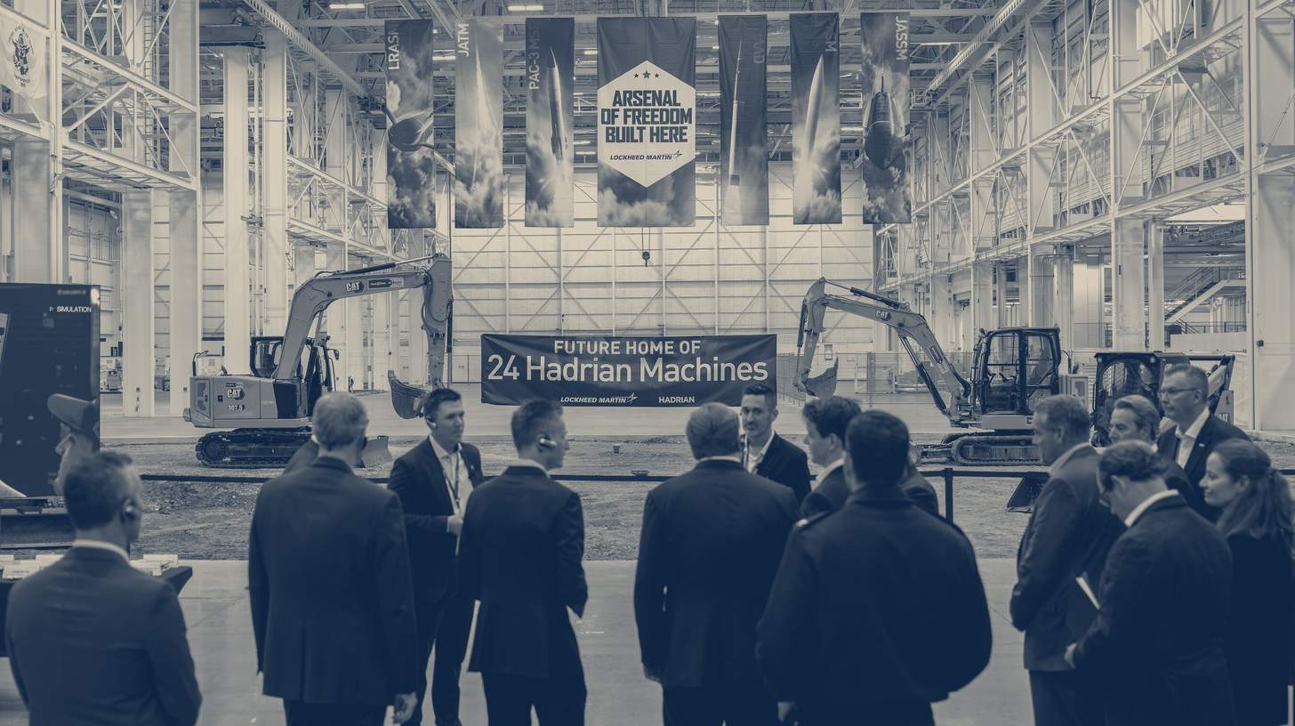 Two-tone Lockheed Martin photo of officials standing in the Grand Prairie, Texas factory hall under a sign marking the future home of 24 Hadrian machines.