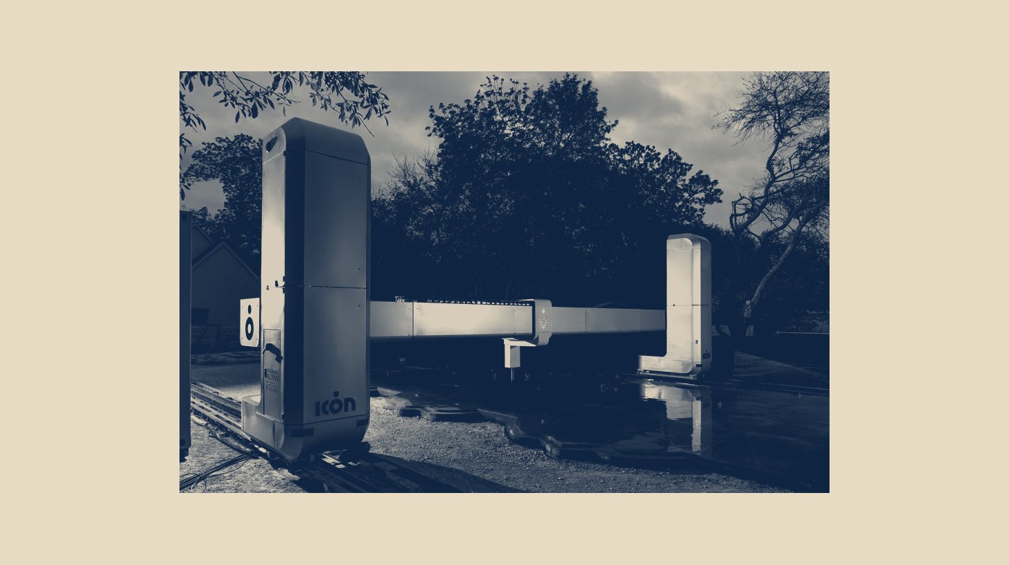 Two-tone ICON Team photo of an ICON next-generation construction printer gantry outdoors, shown at native size as a panel on a plain sand background.