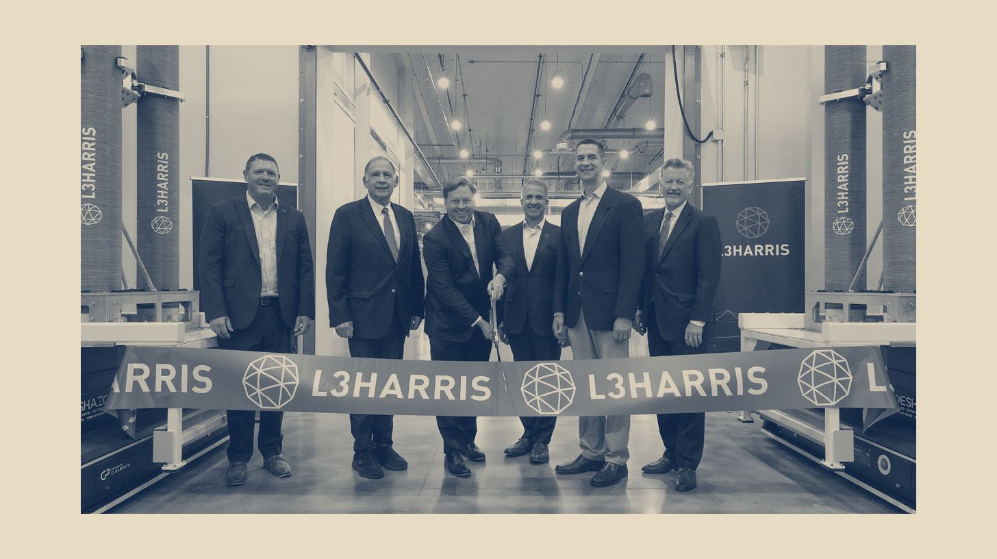 Two-tone L3Harris company photo of officials cutting a ribbon inside the new Camden, Arkansas solid rocket motor facility, shown as a panel on a plain sand background.