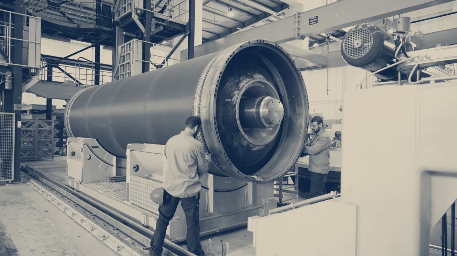 Two-tone photo of two Avio workers beside a large solid rocket motor case on a handling machine at Avio's plant in Italy.