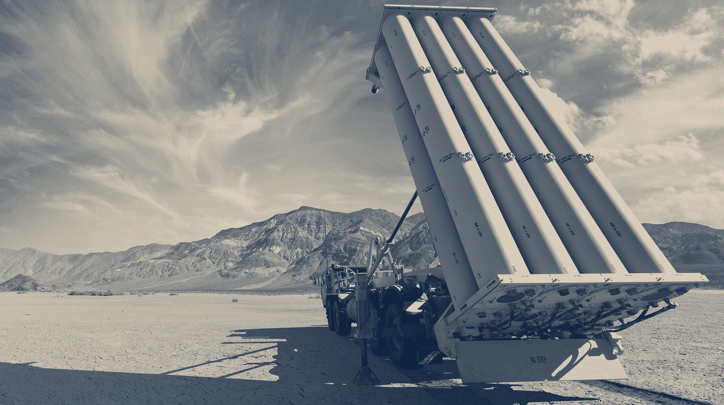 Two-tone Lockheed Martin photo of a THAAD launcher with its missile pack raised on a desert range, mountains behind.