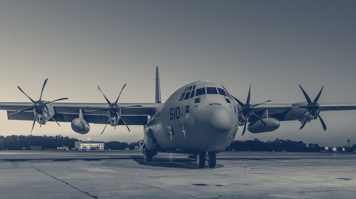 Two-tone Lockheed Martin photo of the C-130J-30 Super Hercules delivered to the U.S. Navy for E-130J conversion, parked on the ramp at dusk.