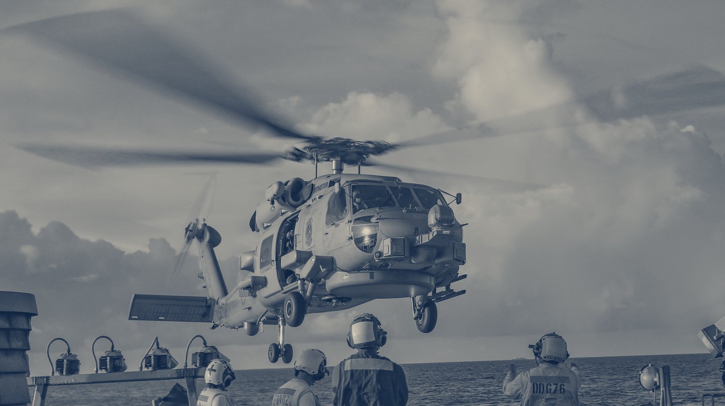 Two-tone U.S. Navy photo of a Royal Australian Navy MH-60R Seahawk lifting off the flight deck of USS Higgins as deck crew watch, South China Sea, October 2022.