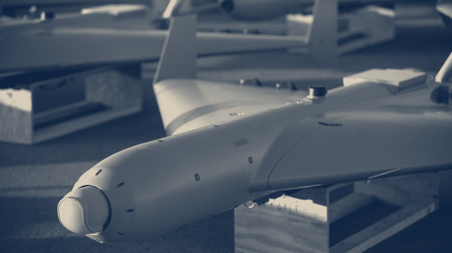 Two-tone U.S. Department of War photo of rows of LUCAS one-way attack drones lined up on a tarmac.