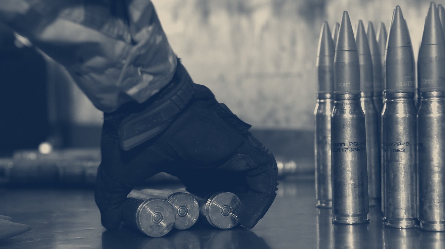 Two-tone U.S. Air National Guard photo of a gloved hand beside a row of 20 mm rounds during an ammunition inspection.