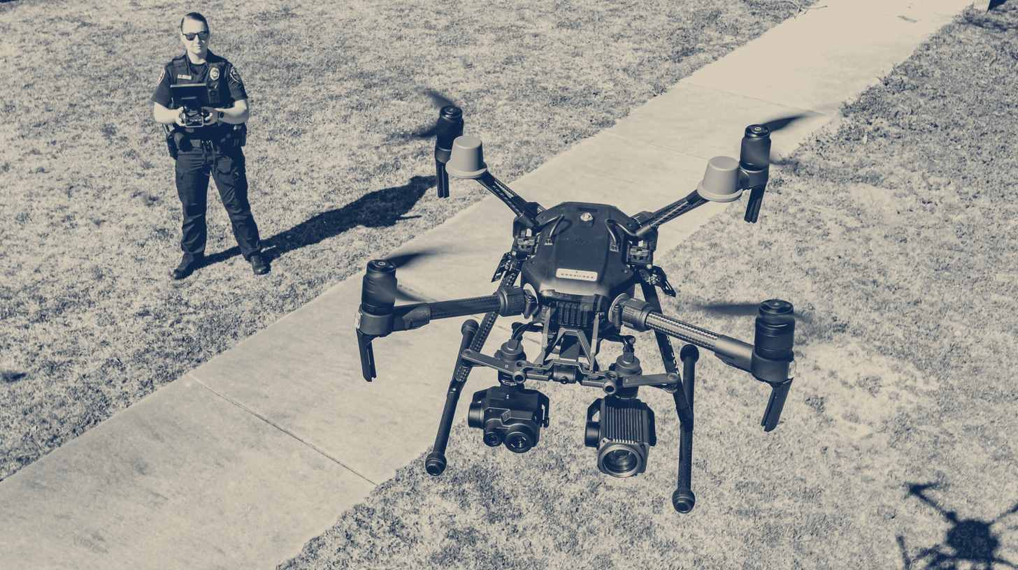 Two-tone photo of a Greenville, North Carolina, police officer standing behind a DJI Matrice drone on the grass before launch.