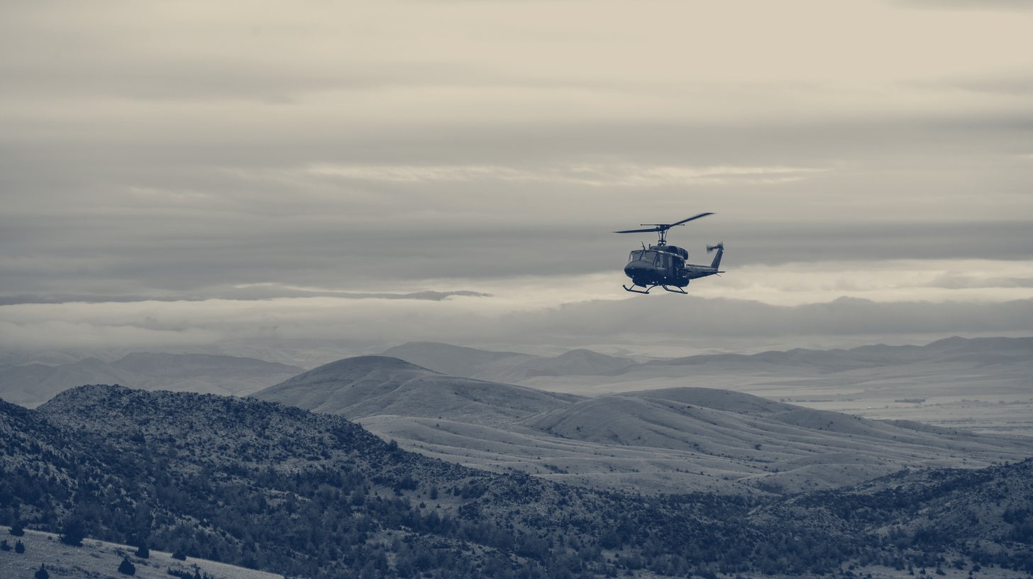 Two-tone U.S. Air Force photo of a UH-1N helicopter flying over the Limestone Hills training range in Montana.