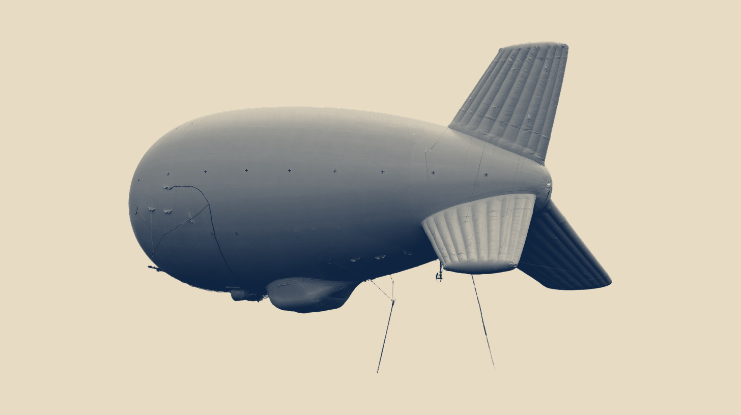 Two-tone U.S. Army photo of a Multi-Domain Task Force tethered aerostat, on a plain sand background.